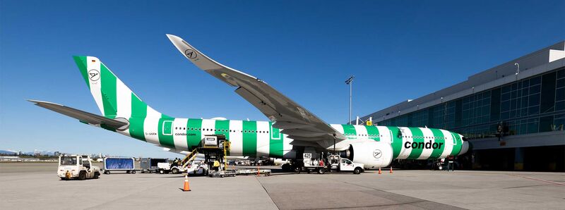 Informationen rund um den Abflughafen Ein grün-weiß gestreiftes Condor Flugzeug steht am Terminal zum Einsteigen bereit